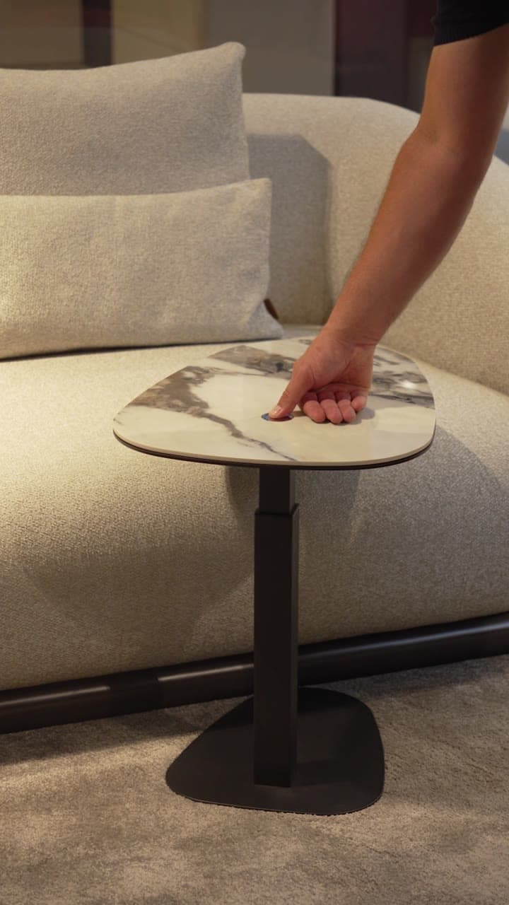 A hand touching the surface of a round marble-look table beside a light-coloured sofa